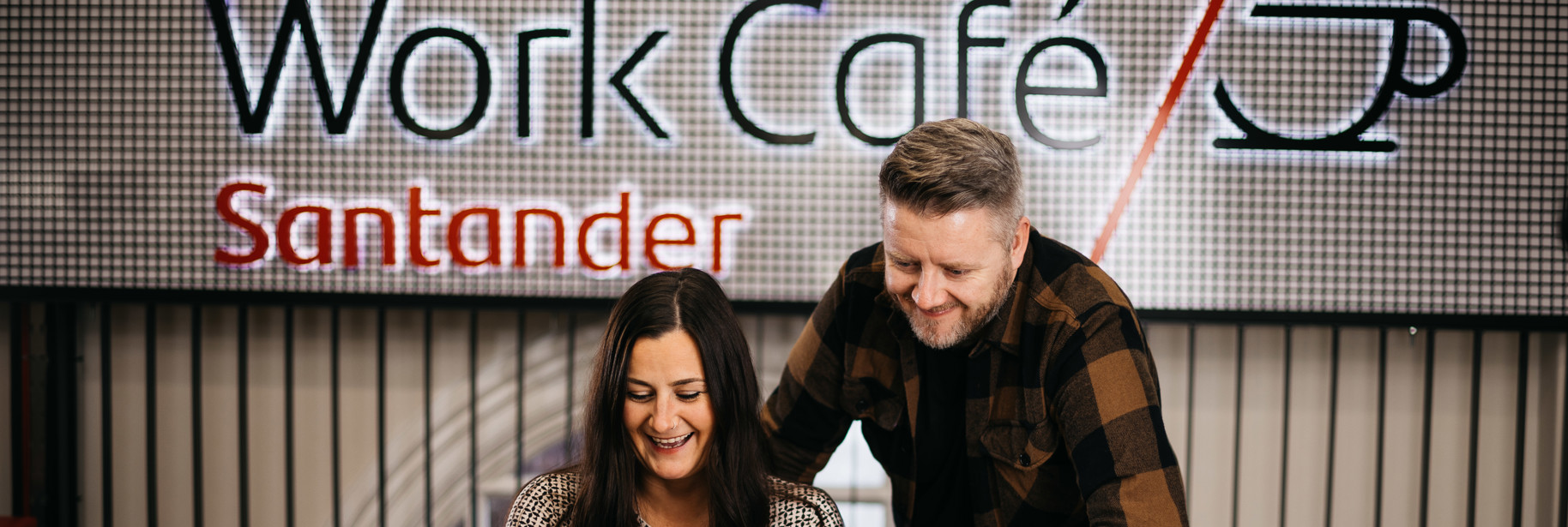 Couple in front of Work Cafe sign on mezzanine of IOM Work Cafe with lap top