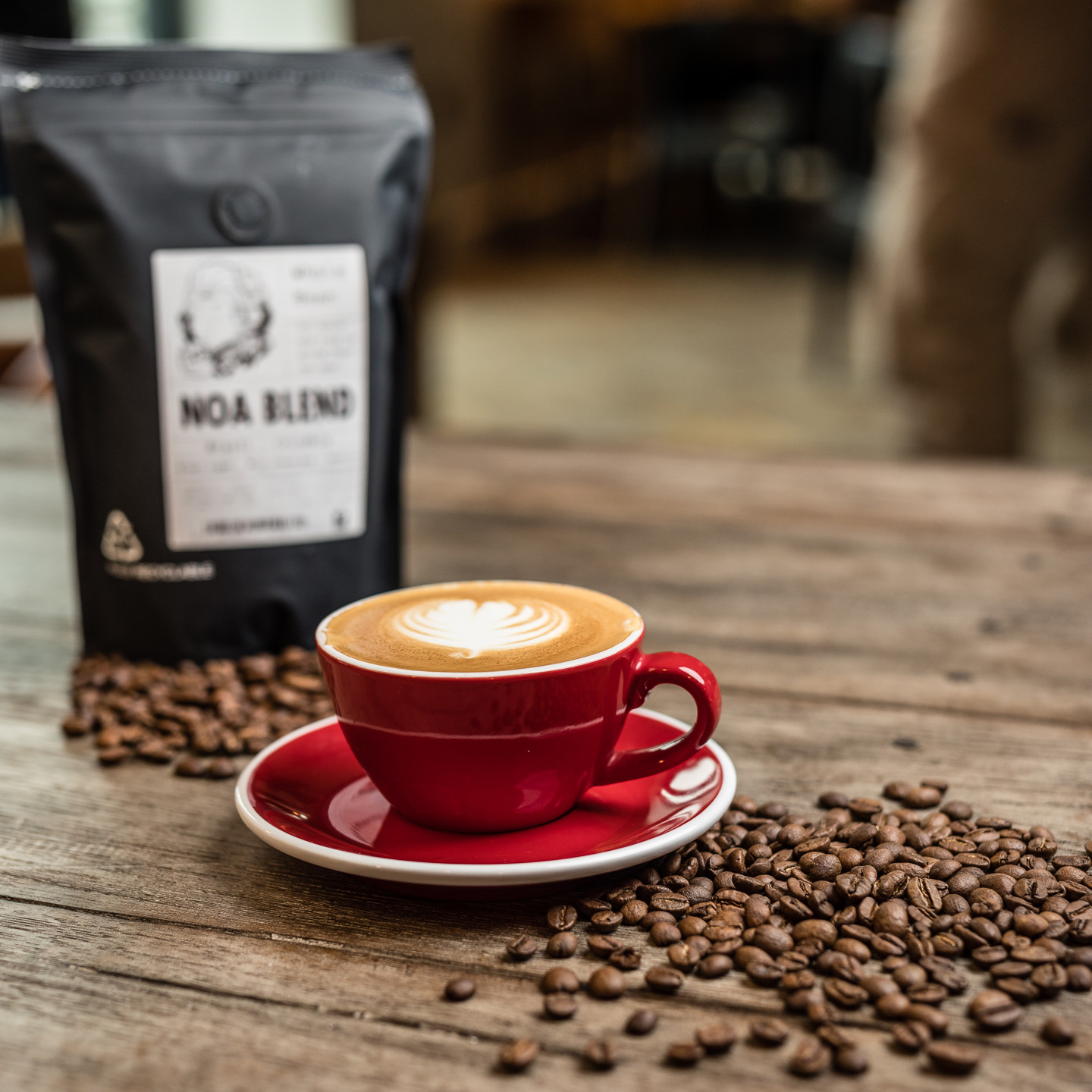 Cup of coffee with bag of Noa coffee beans and loose coffee beans on table