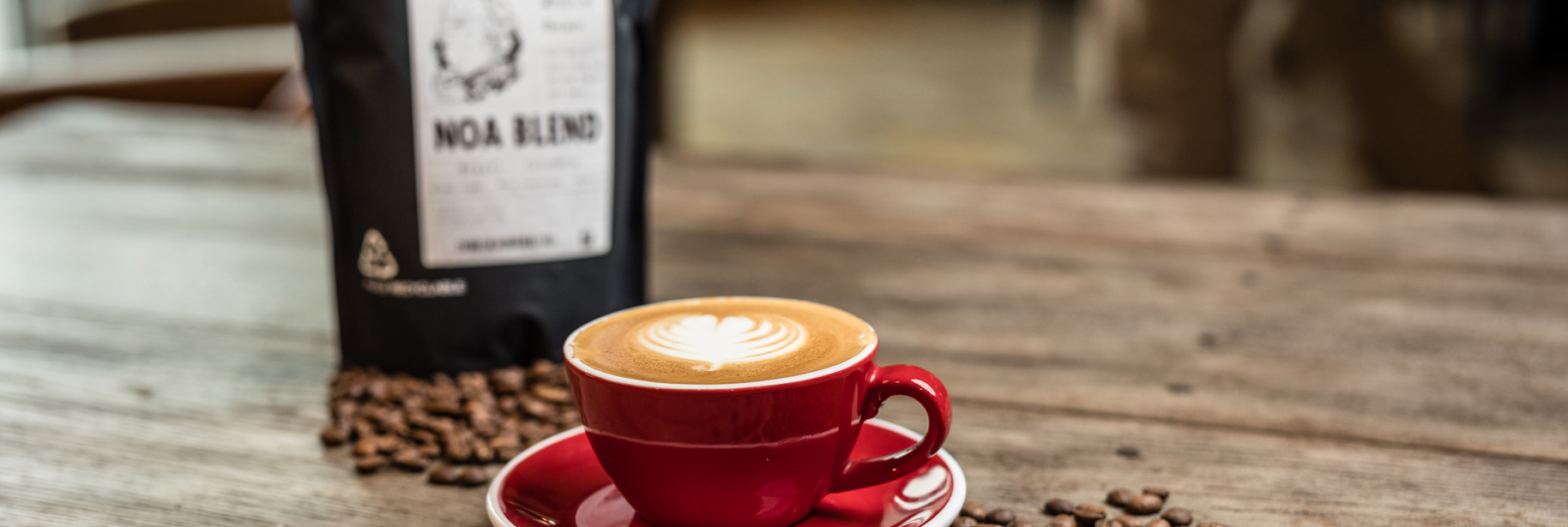 Cup of coffee with bag of Noa coffee beans and loose coffee beans on table
