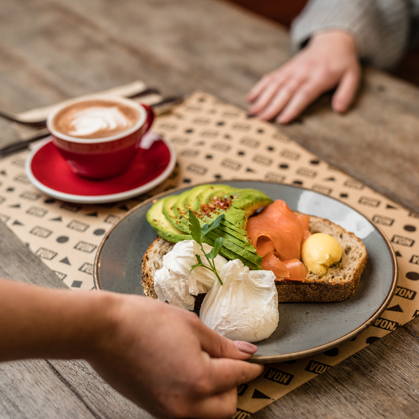 Smoked salmon and poached eggs on sourdough being served with cup of coffee