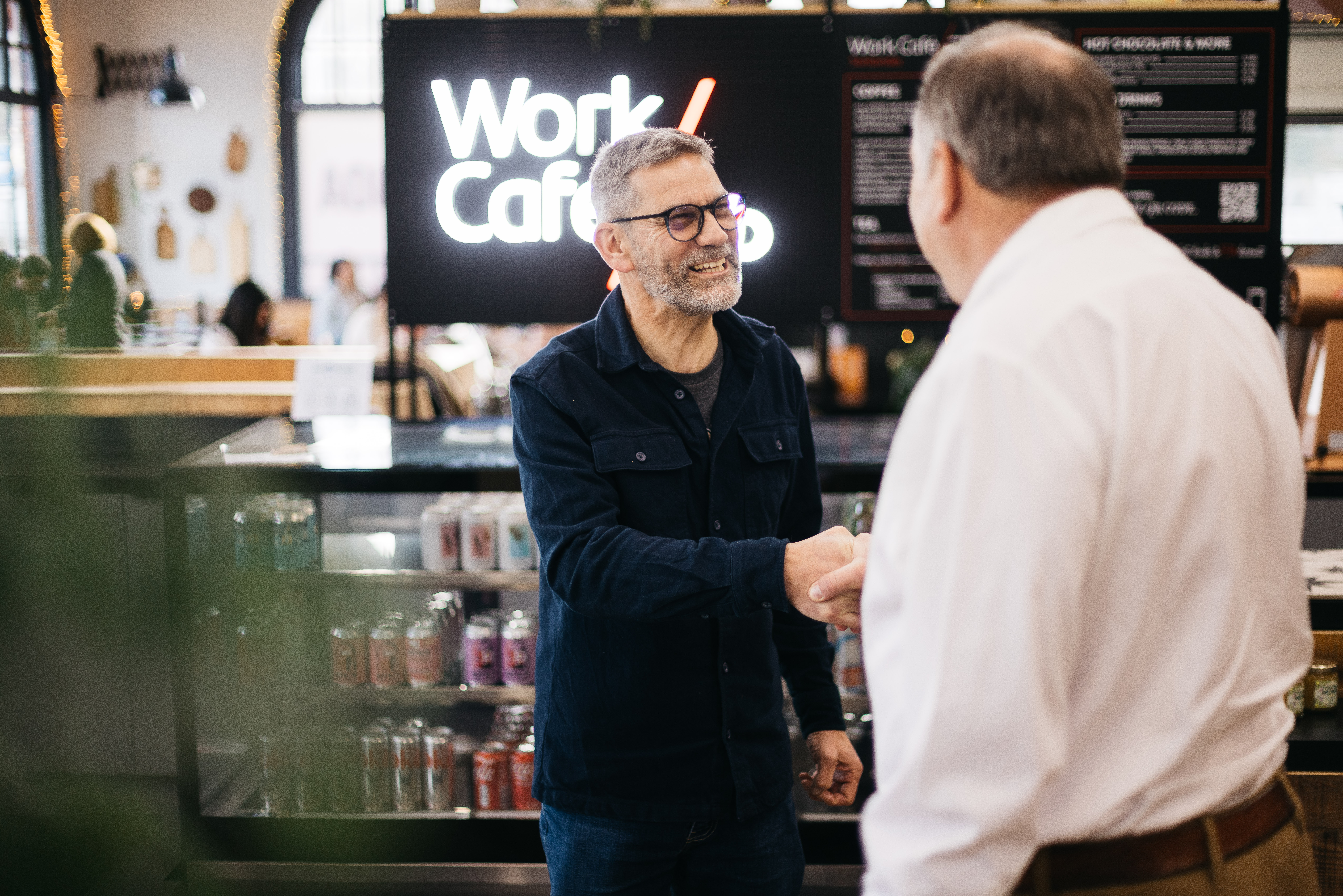 2 men greeting in front of IOM Work Cafe barista counter