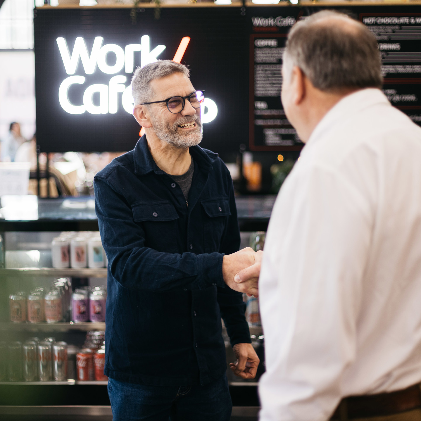 2 men greeting in front of IOM Work Cafe barista counter